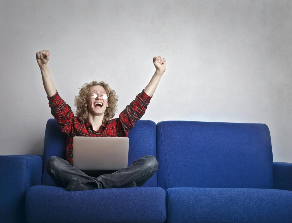 A woman celebrating on a couch while using her laptop.